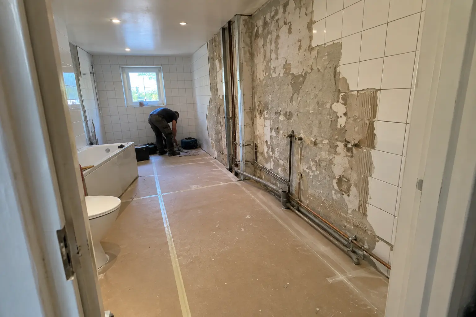 Badrum mitt i renovering utan bygglov, med nedslaget kakel och en person som arbetar i bakgrunden